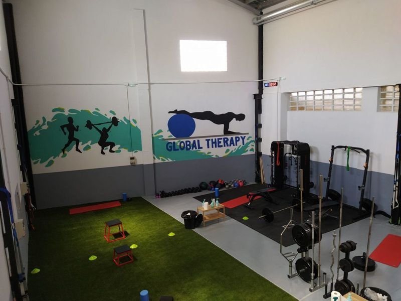 Gimnasio de Global Therapy Mallén con césped, cajones, racks y el mural con el logo del centro